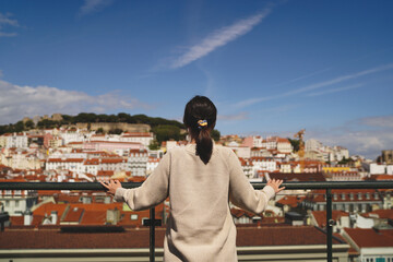 Traveling in Portugal. Young traveling woman enjoying old town Lisbon view, red tiled roofs, ancient architecture and sea view.
