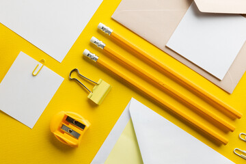 Flat lay of yellow pencils, pen and highlighter and white paper with copy space on yellow background