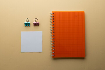 Flat lay of orange notebook, memo note and paper clips with copy space on yellow background