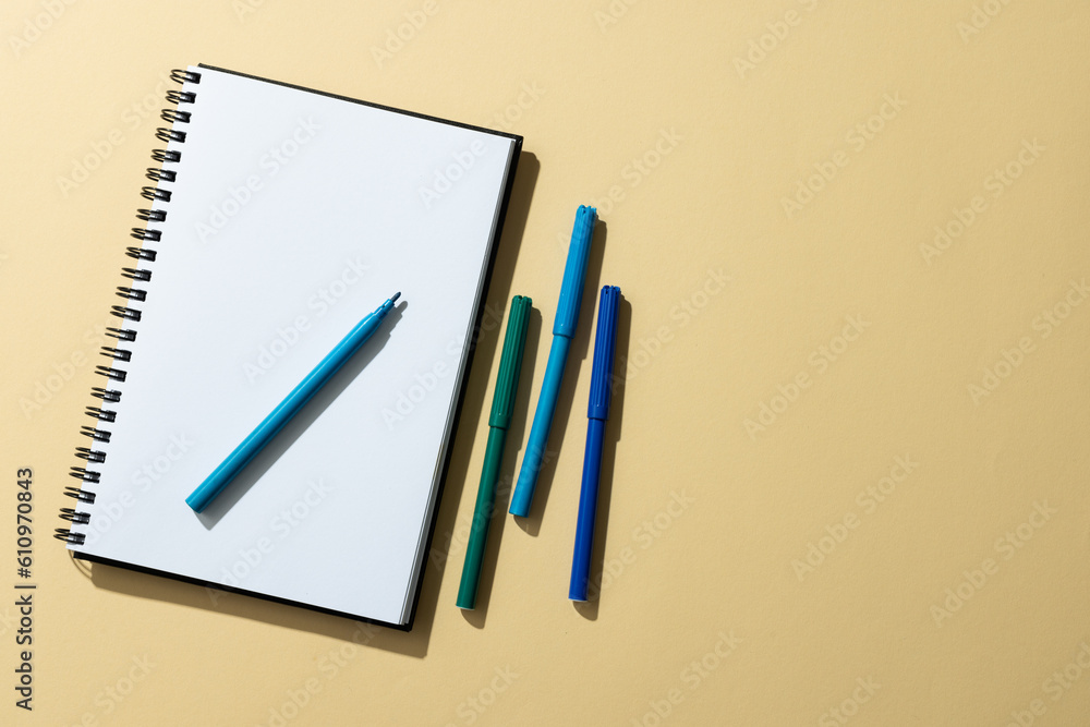 Poster close up of notebook and four markers with copy space on yellow background