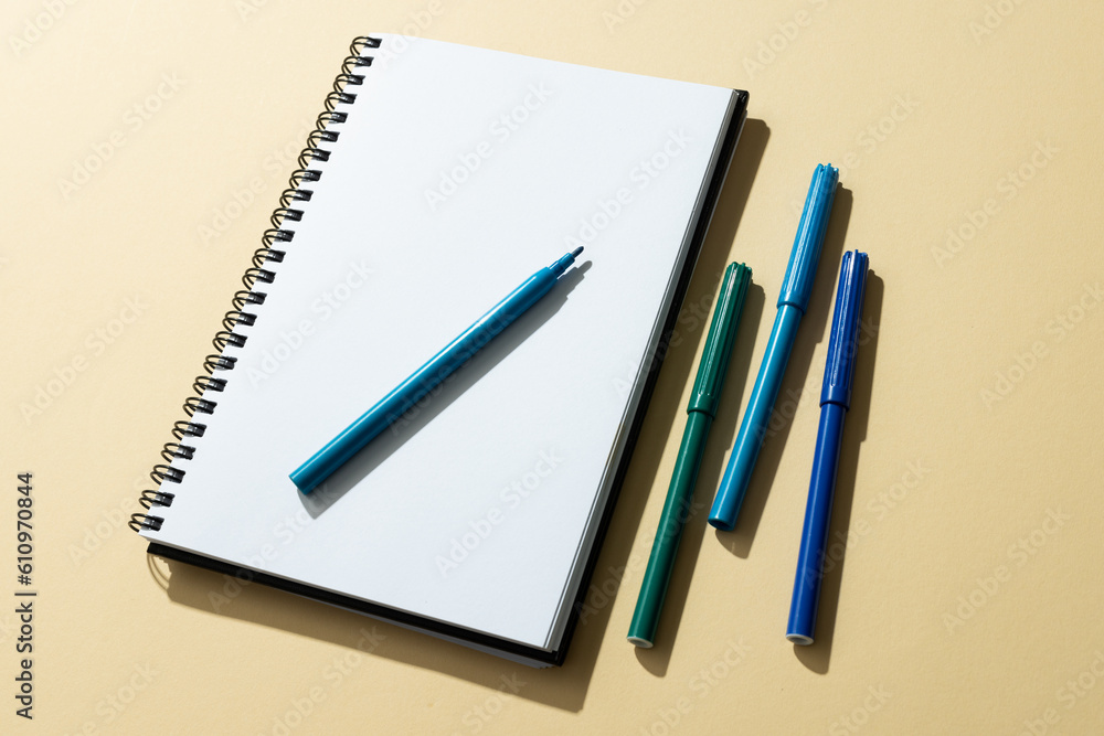 Poster close up of notebook and four markers with copy space on yellow background
