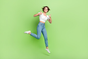 Fototapeta na wymiar Full size photo of excited carefree girl jumping hands fingers demonstrate thumb up empty space isolated on green color background