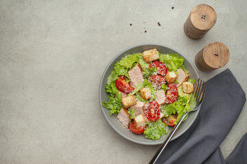 Vegetable salad with chicken and cheese on a gray table. Caesar salad in a gray plate.