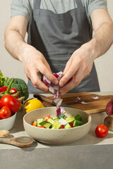 A man prepares a vegetable salad with a whole apron, close-up