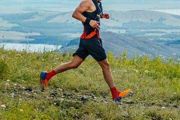 male runner running marathon trail race in background of mountains and lake, summer ultramarathon