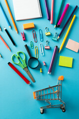 Close up of miniature shopping trolley with school materials on blue background