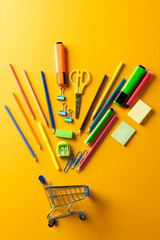Close up of miniature shopping trolley with school materials on orange background