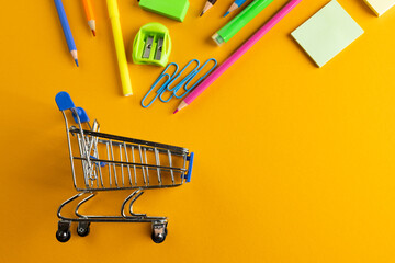 Close up of miniature shopping trolley with school materials, copy space on orange background