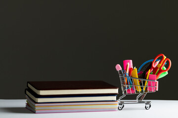 Close up of miniature shopping trolley school materials, books and copy space on grey background