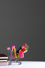 Close up of miniature shopping trolley school materials, books and copy space on grey background