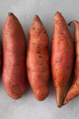 Raw sweet potatoes on a grey background. Orange kumara, yam. Healthy eating.