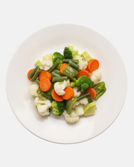 boiled, steamed vegetables on a white plate, top view