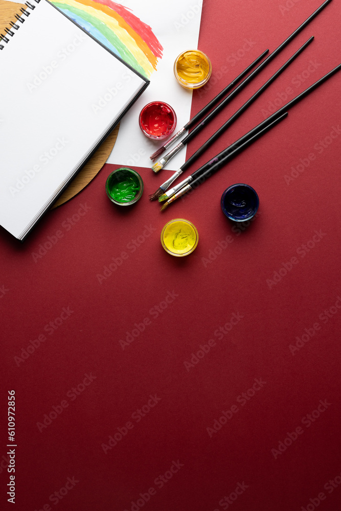 Aufkleber close up of paints, brushes and notebook with copy space on red background