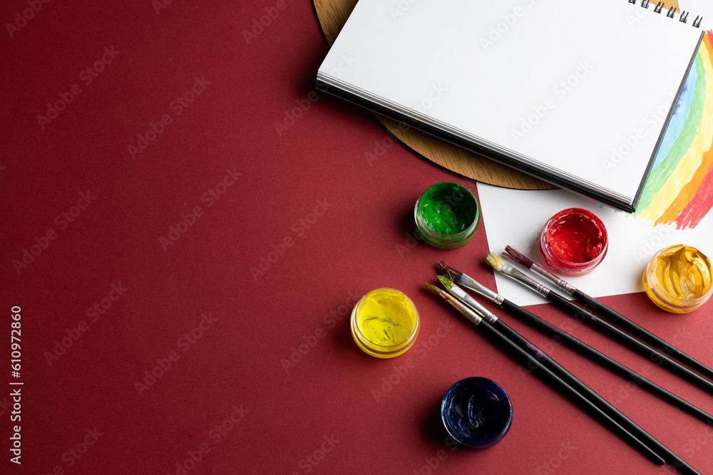 Poster close up of paints, brushes and notebook with copy space on red background