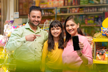 Happy family showing empty smartphone Screen at grocery shop.
