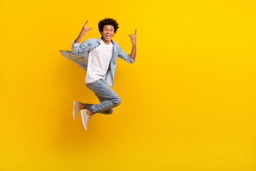 Fototapeta na wymiar Full size photo of active overjoyed man jumping demonstrate heavy metal symbol isolated on yellow color background
