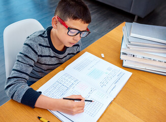 Boy, student and writing in book for math, studying or homework for learning, assessment or education on table. Smart kid, young child and busy reading mathematics textbook, problem solving and focus