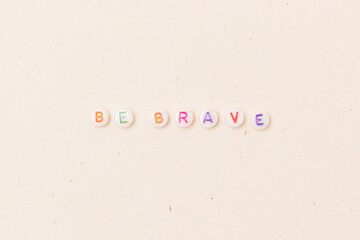 Be brave. Quote made of white round beads with multicolored letters on a beige background.