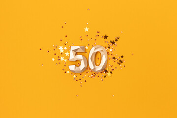 Gold colored number 50 and stars confetti on a yellow background. Festive compisition.
