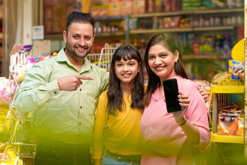 Happy family showing empty smartphone Screen at grocery shop.