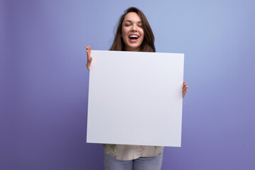 positive young brunette woman showing advertisement on white sheet - obrazy, fototapety, plakaty