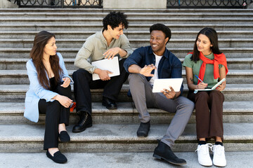Fototapeta premium Group of smiling multiracial students using digital tablet, studying together sitting in university campus, education. Happy friends talking, communication, sharing ideas outdoors. Diversity concept