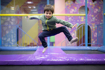 Little boy jumping and having fun on trampoline in amusement center for kids