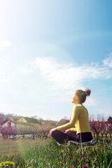 Woman meditating outdoors in countryside, yoga on green grass in village.