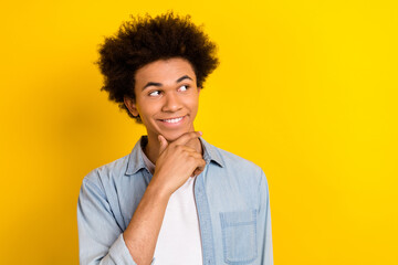 Fototapeta na wymiar Portrait of cheerful satisfied minded guy wear jeans jacket looking at offer empty space arm on chin isolated on yellow color background