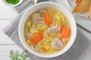 Chicken soup with noodles and vegetables in white bowl on a wooden background.