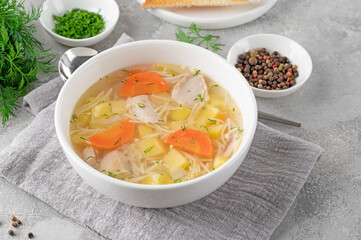 Chicken soup with noodles and vegetables in white bowl on a gray concrete background.