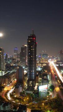 Vertical timelapse of night Bangkok, the capital of Thailand. Transport traffic in illuminated streets with urban architecture