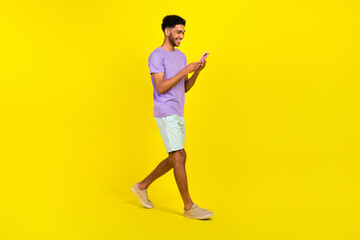 Fototapeta na wymiar Full body cadre of guy texting his friends chatting smartphone walking streets use facebook messenger isolated on yellow color background
