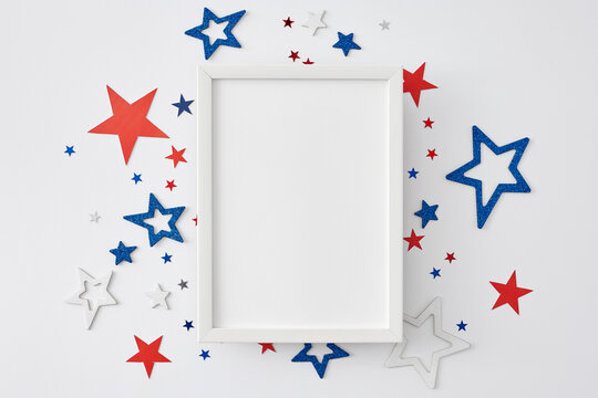 4th of July celebration theme. Top view flat lay of patriotic star-shaped confetti on white background with blank frame for text or greeting