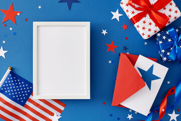 Ready yourself for an Independence Day blowout. Top view flat lay of gift boxes, postcard, american flag, patriotic ribbons, sparkles on blue background with blank frame for message or greeting