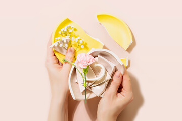 Female hands holding pieces of broken plate with tender flower on pink background. Concept or...