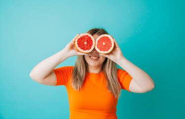 Beautiful portrait of a young woman with long blond hair, standing isolated on a blue background, with orange slices.gummy smile