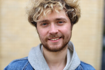 Happy curly blond guy with beard smiling on beige background.