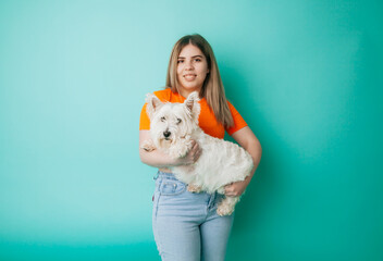 portrait of a beautiful young girl with a dog in her arms on a blue background, the girl hugs her pet West Highland White Terrier, copy space