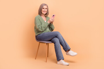 Fototapeta na wymiar Full length body of sit relaxed chair grandmother exploring new technologies use phone browsing google isolated on beige color background