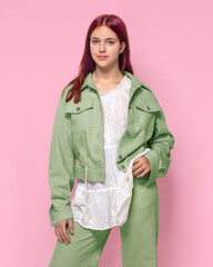 A girl in a light green oversized denim suit on a pink background studio isolated.