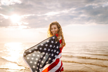 Young woman with  American flag on the beach. Patriotic holiday. USA celebrate 4th of July....