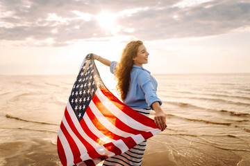 Young woman with  American flag on the beach. Patriotic holiday. USA celebrate 4th of July....