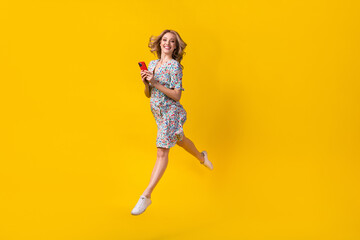 Fototapeta na wymiar Full body photo of jump careless young girl shopaholic running with smartphone web store order clothes isolated on yellow color background