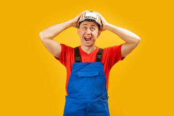 Fototapeta premium Young architect man with helmet with shocked facial expression, isolated yellow background . Worker or builder holding his head and screaming