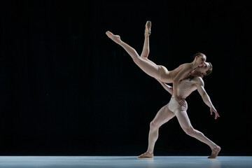 Graceful performance. Talented, artistic young woman and man, ballet dancers dancing against black...