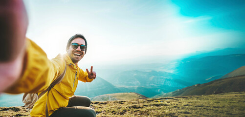 Young hiker man taking selfie portrait on the top of mountain - Happy guy smiling at camera - Tourism, sport life style and social media influencer concept - obrazy, fototapety, plakaty