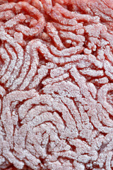 Frozen thawing red raw minced meat or ground beef, close-up macro view from above with abstract ice crystals texture and pattern