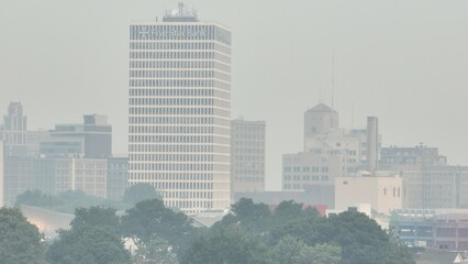 Fototapeta premium Poor air quality in Rochester NY caused by Canadian wildfire smoke over the city skyline dense around downtown office buildings due to climate change conditions in Canada