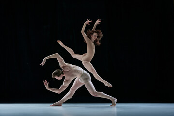 Graceful, artistic couple, man and woman, professional ballet dancers performing against black...